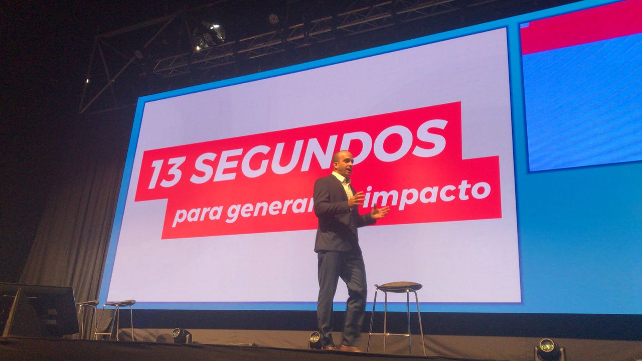 Facilitador da Axya conduzindo uma palestra em palco para uma plateia corporativa